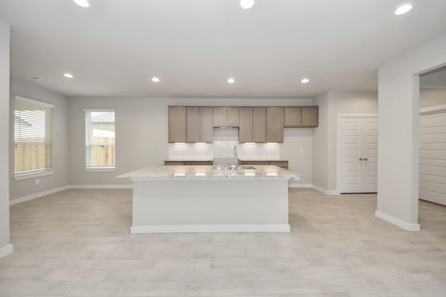 kitchen featuring decorative backsplash, sink, light stone countertops, and a kitchen island with sink