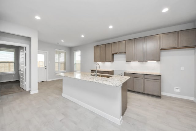 kitchen featuring a wealth of natural light, light stone counters, a kitchen island with sink, and sink