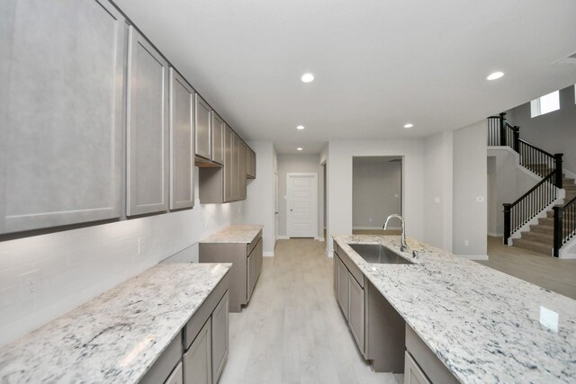 kitchen featuring light wood-type flooring, light stone countertops, sink, and tasteful backsplash