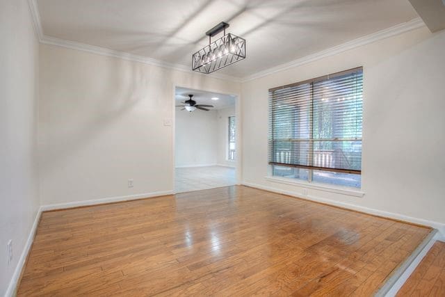 empty room with ceiling fan with notable chandelier, light hardwood / wood-style floors, and crown molding