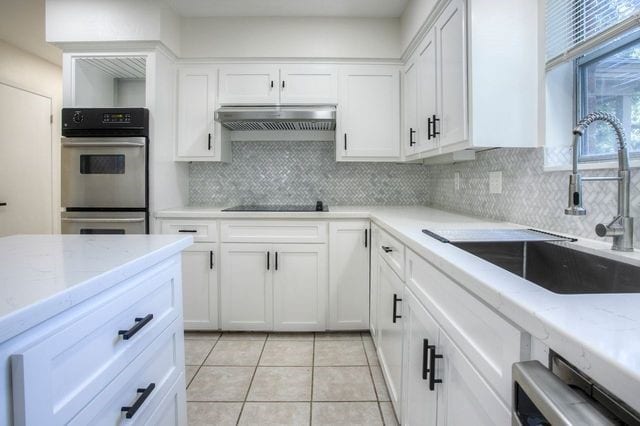 kitchen with double oven, black electric cooktop, under cabinet range hood, a sink, and tasteful backsplash