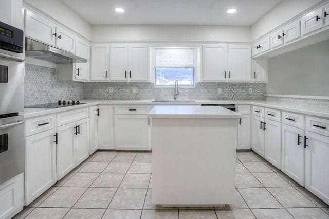 kitchen with black electric stovetop, tasteful backsplash, light tile patterned floors, a kitchen island, and white cabinets