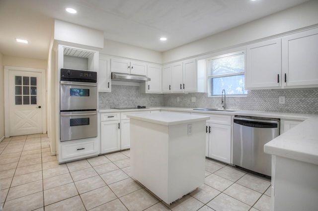 kitchen with white cabinetry, backsplash, light tile patterned floors, stainless steel appliances, and a kitchen island