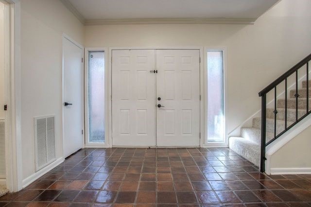 foyer with stairway, baseboards, visible vents, and ornamental molding