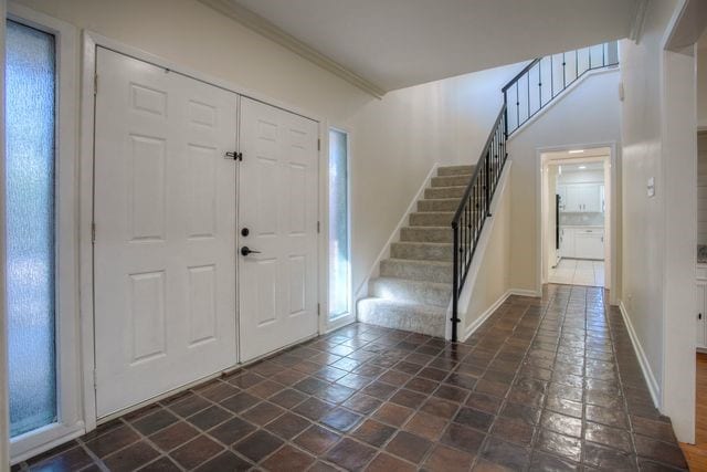 entrance foyer with baseboards, stone tile flooring, stairway, and crown molding
