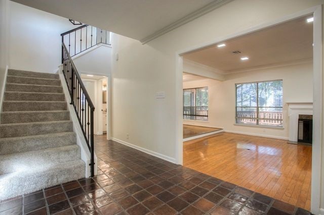 staircase featuring baseboards, recessed lighting, a fireplace with raised hearth, stone finish flooring, and ornamental molding