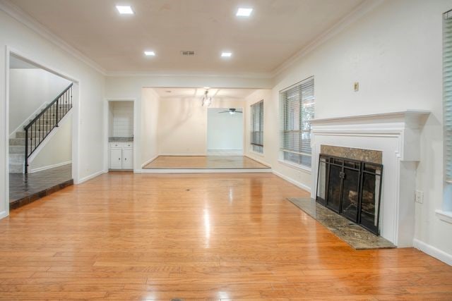 unfurnished living room with a high end fireplace, crown molding, light wood finished floors, and ceiling fan