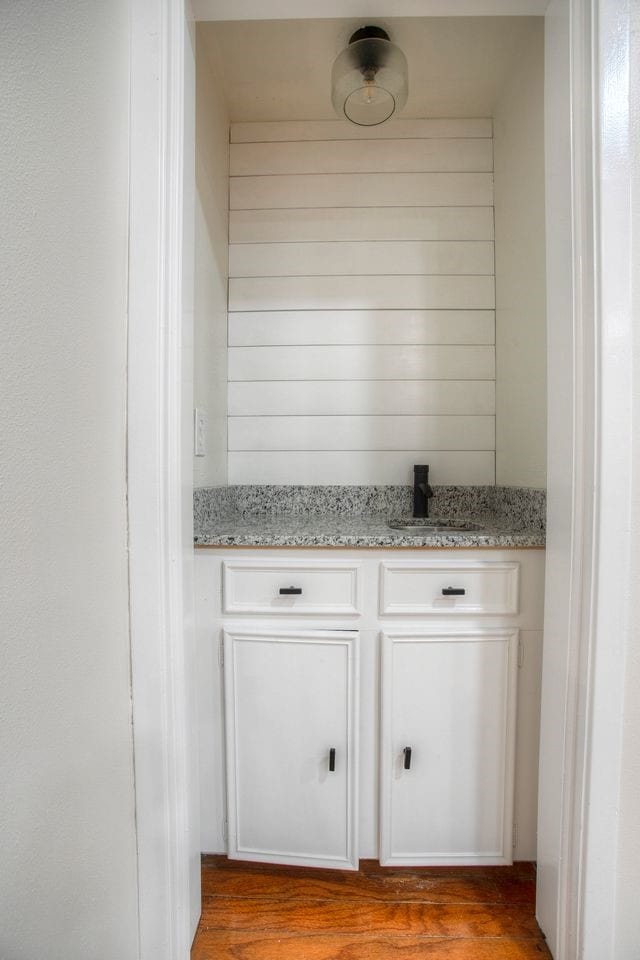 bar with wood walls, light stone counters, sink, and wood-type flooring