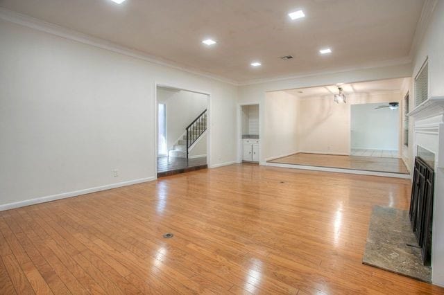 unfurnished living room with stairway, light wood finished floors, crown molding, baseboards, and a fireplace
