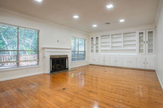 unfurnished living room featuring a high end fireplace, baseboards, crown molding, and wood finished floors