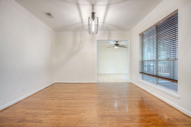 unfurnished dining area featuring baseboards, visible vents, a ceiling fan, wood finished floors, and ornamental molding