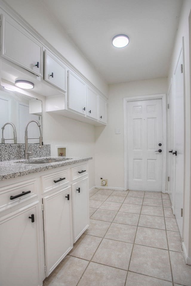 laundry room with hookup for a washing machine, a sink, light tile patterned floors, cabinet space, and baseboards