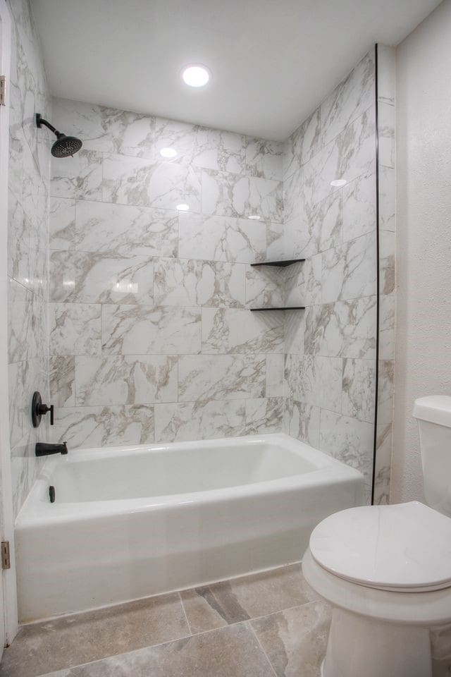 bathroom with stone tile flooring, toilet, and shower / washtub combination