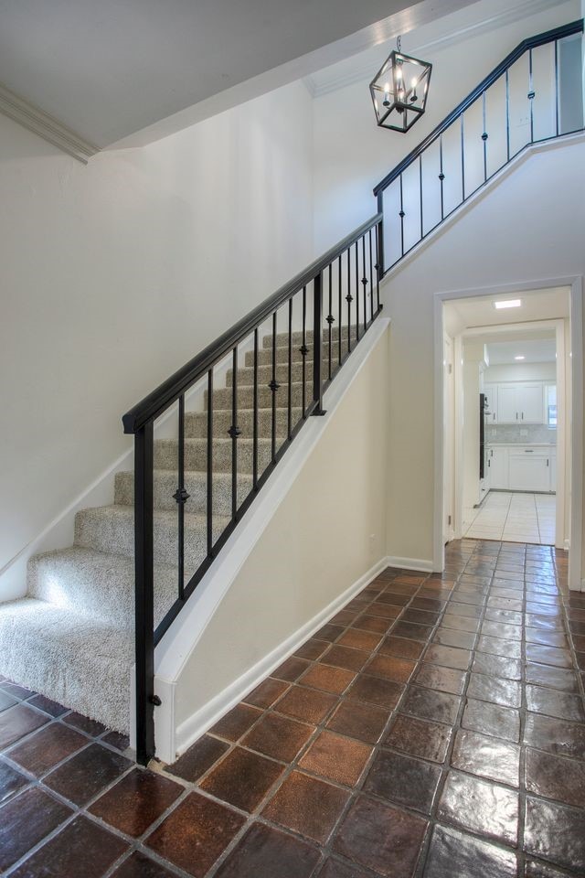 staircase featuring stone tile flooring, baseboards, crown molding, and a chandelier