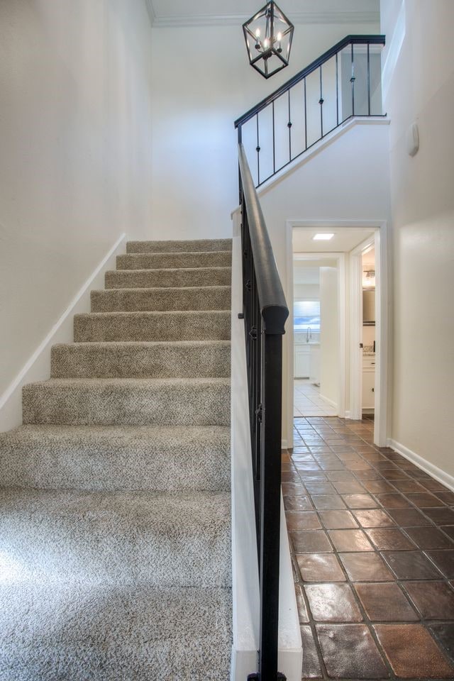 stairs with crown molding, a high ceiling, and an inviting chandelier