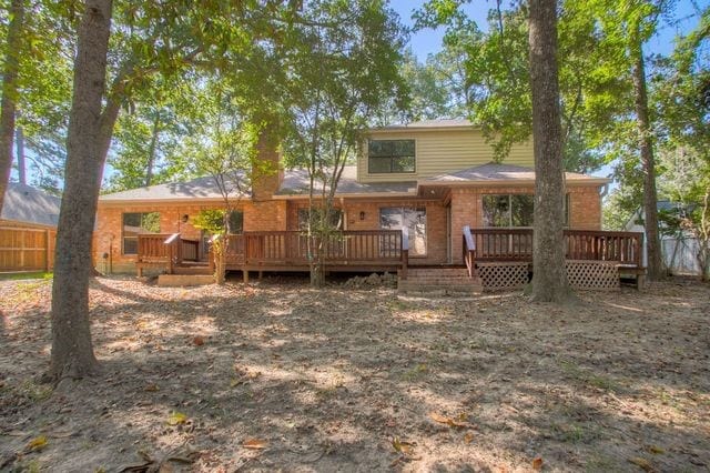 back of property featuring fence, a wooden deck, and brick siding