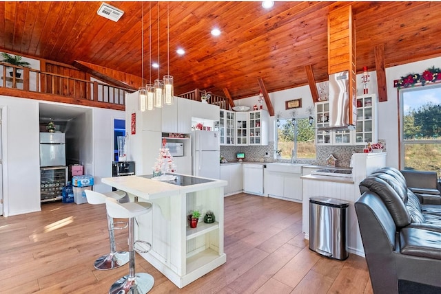 kitchen featuring white cabinets, vaulted ceiling, light wood-type flooring, white fridge, and a kitchen island