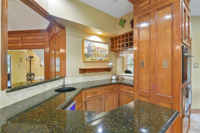 kitchen with dark stone counters, tasteful backsplash, kitchen peninsula, sink, and light tile patterned flooring