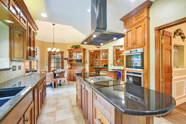 kitchen featuring dark stone countertops, a center island, a notable chandelier, island exhaust hood, and double oven