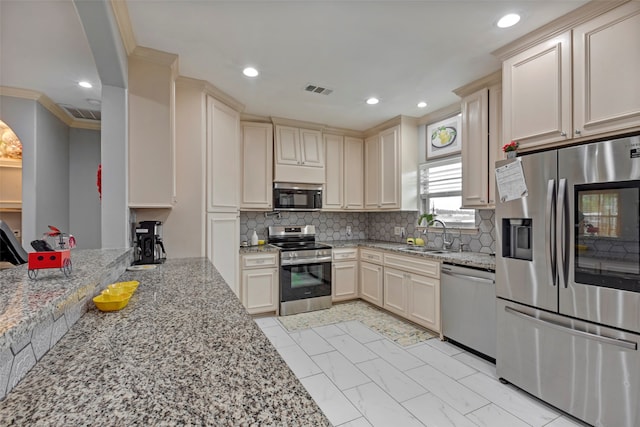 kitchen with light stone counters, stainless steel appliances, sink, and cream cabinetry