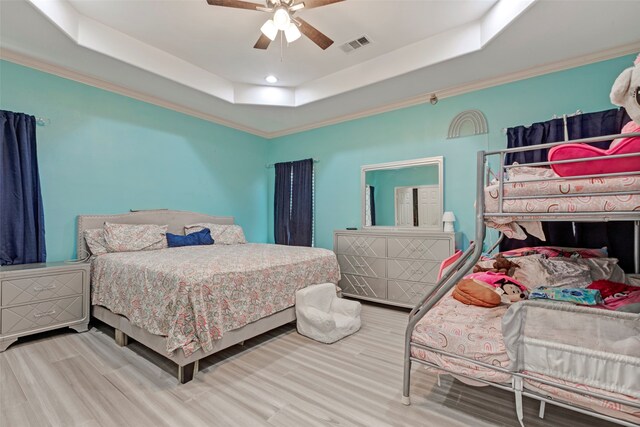 bedroom with a tray ceiling, crown molding, wood-type flooring, and ceiling fan