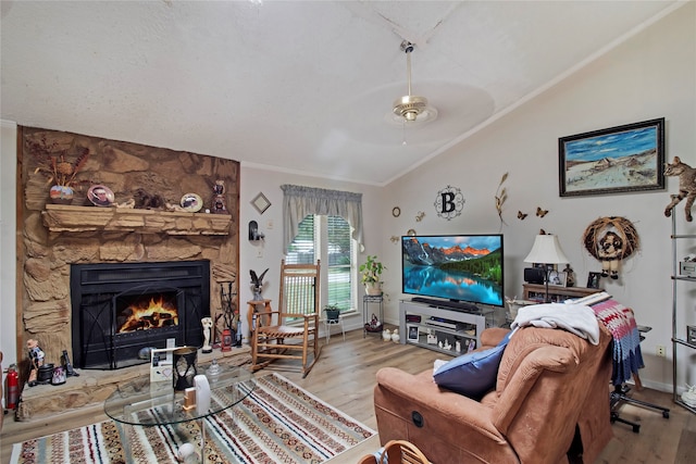 living room featuring crown molding, vaulted ceiling, light hardwood / wood-style floors, a stone fireplace, and ceiling fan