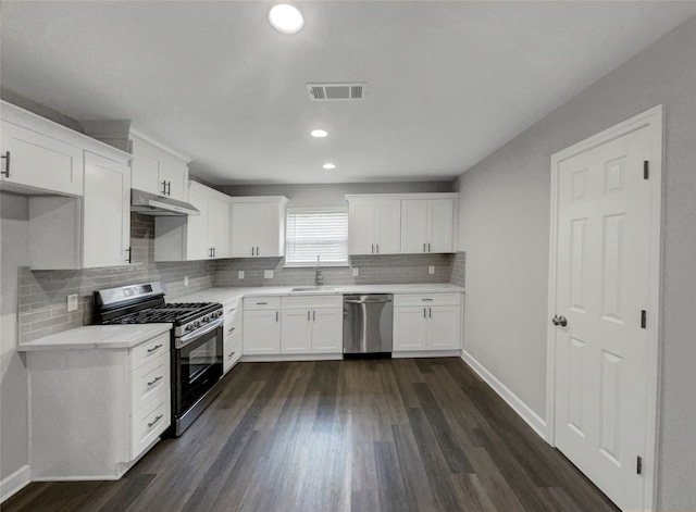 kitchen with dark hardwood / wood-style flooring, backsplash, appliances with stainless steel finishes, sink, and white cabinetry