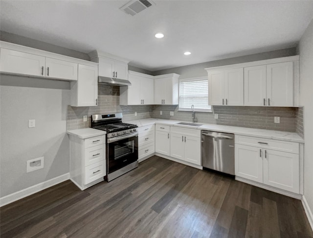 kitchen with appliances with stainless steel finishes, dark hardwood / wood-style flooring, white cabinetry, sink, and tasteful backsplash