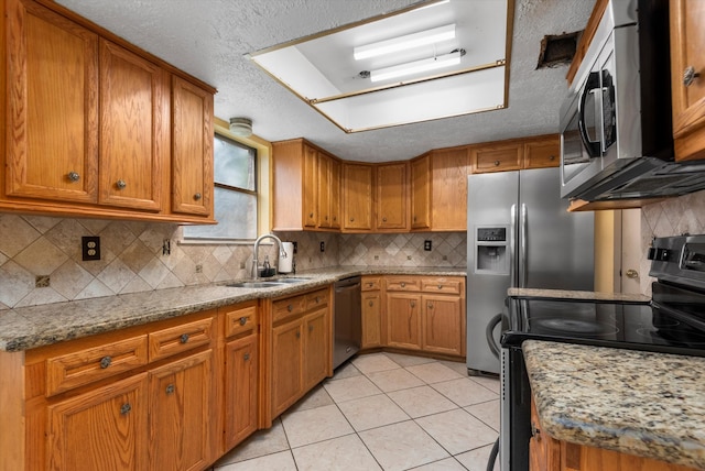 kitchen with sink, stainless steel appliances, light stone counters, backsplash, and light tile patterned floors