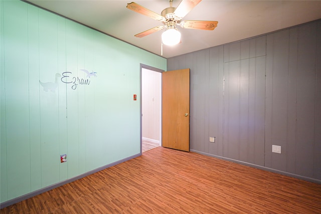 empty room featuring ceiling fan, wood walls, and wood-type flooring