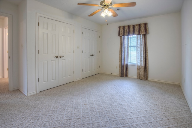 unfurnished bedroom with ceiling fan, light carpet, and multiple closets