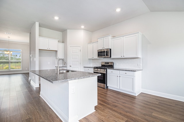 kitchen with white cabinetry, sink, dark stone countertops, stainless steel appliances, and a center island with sink