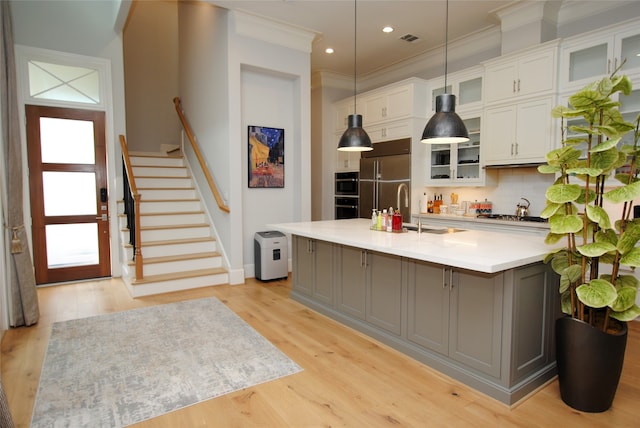 kitchen featuring light wood-type flooring, white cabinets, hanging light fixtures, and an island with sink