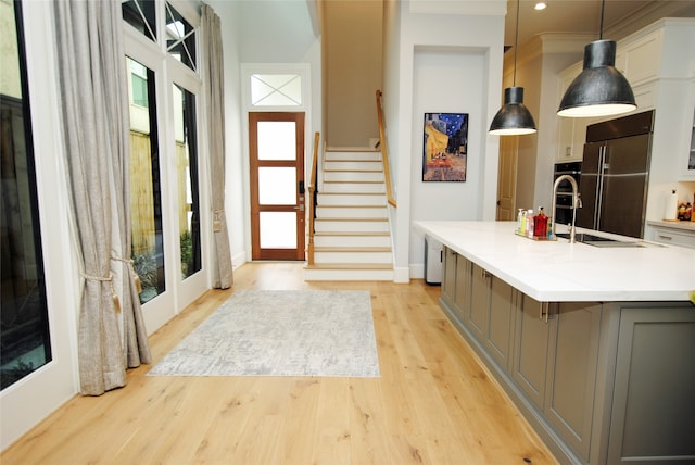 interior space featuring built in fridge, an island with sink, hanging light fixtures, light wood-type flooring, and white cabinets