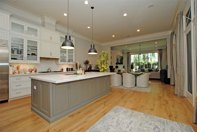 kitchen with hanging light fixtures, light wood-type flooring, white cabinetry, a kitchen island with sink, and ornamental molding