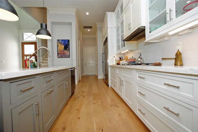 kitchen with light hardwood / wood-style floors, white cabinetry, sink, pendant lighting, and ornamental molding