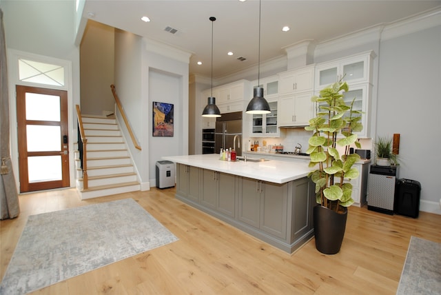 kitchen featuring decorative light fixtures, light hardwood / wood-style floors, a kitchen island with sink, crown molding, and white cabinetry