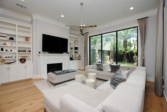 living room with light wood-type flooring, ornamental molding, and built in shelves