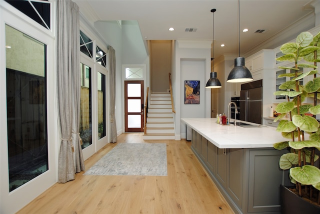 kitchen featuring white cabinets, decorative light fixtures, light wood-type flooring, built in fridge, and an island with sink