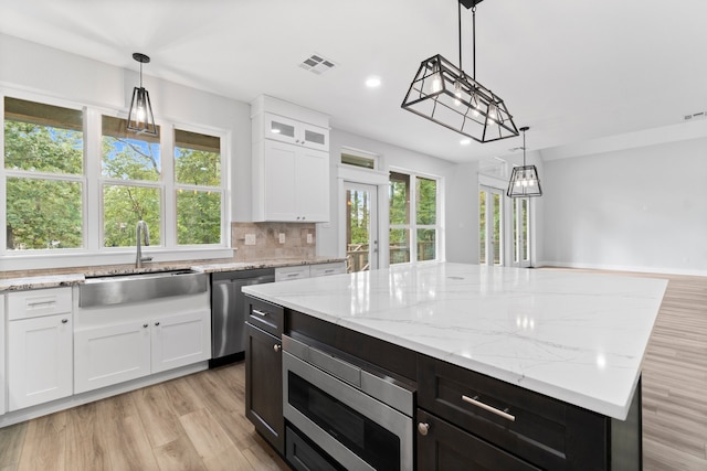 kitchen featuring white cabinetry, decorative light fixtures, a center island, sink, and appliances with stainless steel finishes