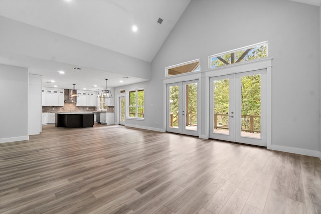 unfurnished living room with high vaulted ceiling, plenty of natural light, light hardwood / wood-style floors, and french doors