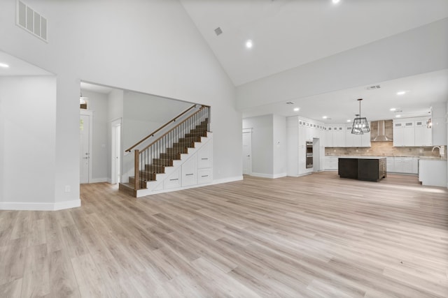 unfurnished living room with high vaulted ceiling, sink, and light hardwood / wood-style flooring