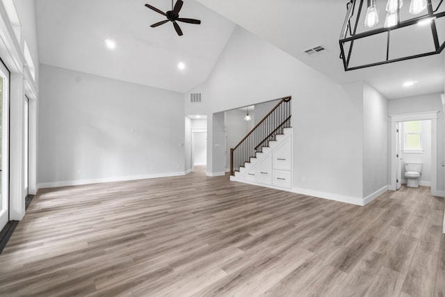 unfurnished living room featuring ceiling fan with notable chandelier, high vaulted ceiling, and light hardwood / wood-style flooring