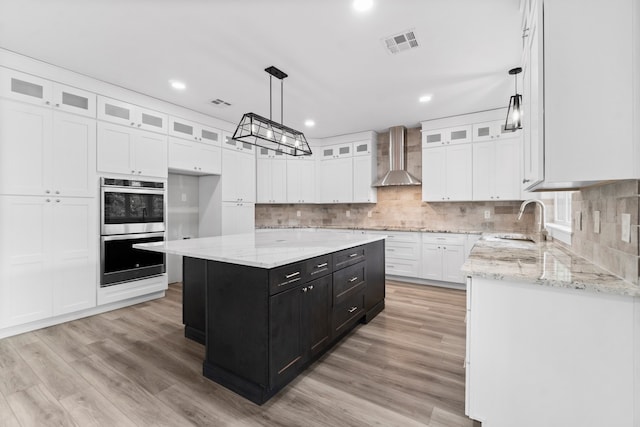 kitchen featuring a center island, pendant lighting, wall chimney exhaust hood, and light hardwood / wood-style floors