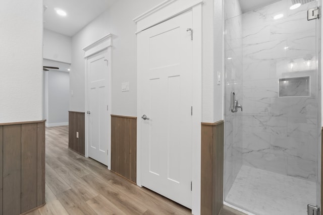 bathroom featuring wood-type flooring, a shower with shower door, and wooden walls