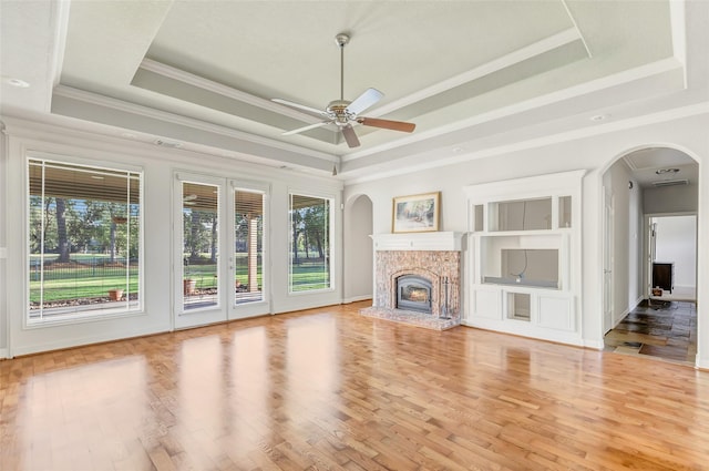 unfurnished living room with ceiling fan, crown molding, a tray ceiling, a fireplace, and hardwood / wood-style flooring