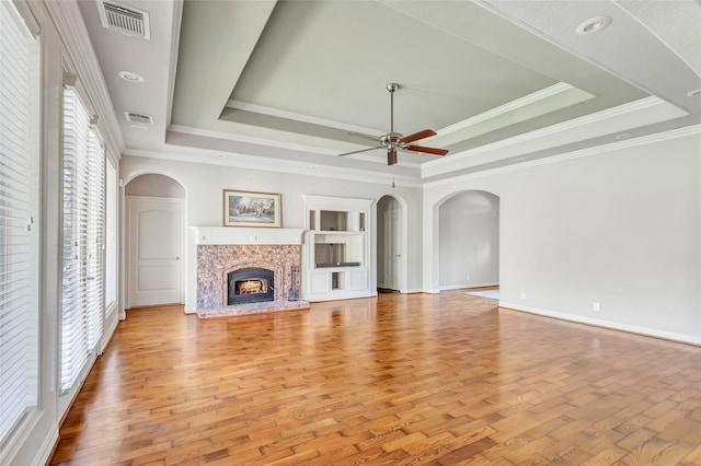 unfurnished living room featuring a fireplace, a tray ceiling, ceiling fan, and light hardwood / wood-style floors