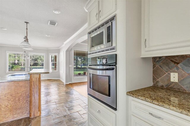 kitchen with light stone countertops, white cabinets, decorative light fixtures, and appliances with stainless steel finishes