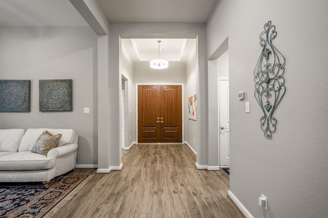 entrance foyer with light wood-style floors, a tray ceiling, a towering ceiling, and baseboards