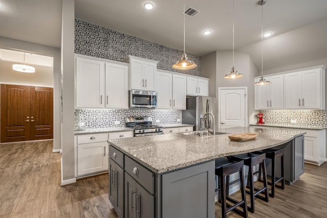 kitchen with visible vents, white cabinets, an island with sink, dark wood-style floors, and appliances with stainless steel finishes